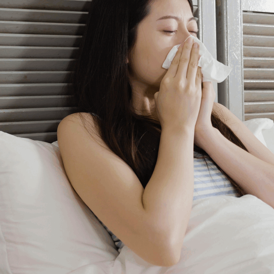 Frau mit Milbenallergie putzt sich im Bett die Nase