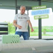 Heiko hinter einem Einzelbett zeigt auf die Matratze im Bett